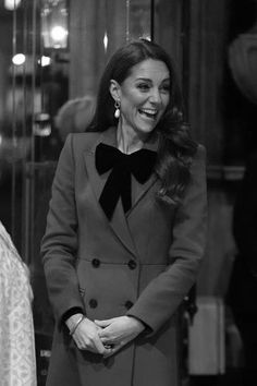 a woman in a coat smiles as she stands next to another woman