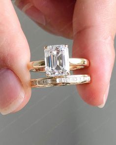 a woman's hand holding an engagement ring with a diamond in the center and two bands around it