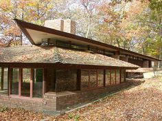 a house in the woods surrounded by trees and leaves with a roof made of bricks