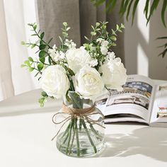 a vase filled with white flowers sitting on top of a table next to an open book