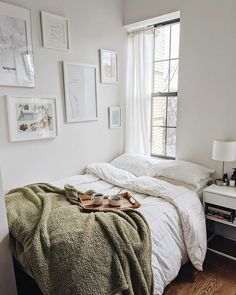 an unmade bed in a white bedroom with pictures on the wall above it and a window