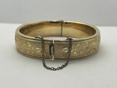 an old gold bracelet with a chain hanging from it's side, on a white surface