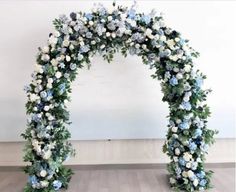 a white and blue floral arch with greenery on the floor in front of a wall