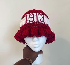 a white mannequin head wearing a red and white knitted hat with the number thirteen on it