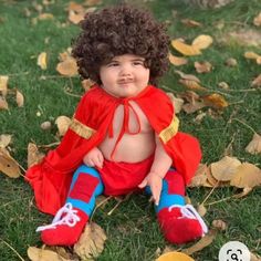 a small child dressed up as superman sitting on the grass with leaves around him and smiling