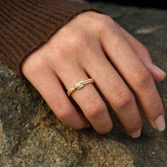 a woman's hand with a diamond ring on top of her finger, resting on a rock