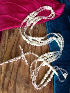 three necklaces on a wooden table with pink and blue material around them, including beads