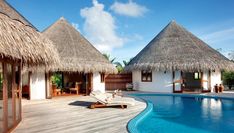 an outdoor swimming pool with thatched roofs and lounge chairs next to the side of it