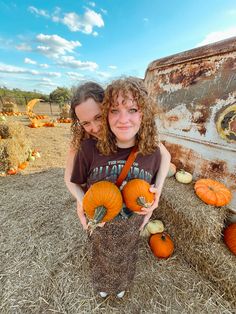 two girls are holding pumpkins in front of a rusted truck and hay bales