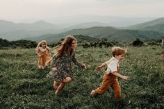 three children running in the grass with mountains in the background