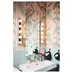 a bathroom with palm trees on the wall and pink tiles, along with two mirrors