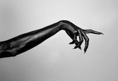 a black and white photo of a person's hand reaching for something in the sky