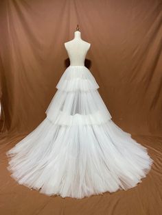 a white wedding dress is displayed on a mannequin stand in front of a brown backdrop