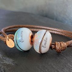 two bracelets with personalized charms on them sitting on a stone surface in front of a rock