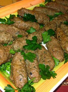 a platter filled with meat and greens on top of a wooden table next to a red cloth