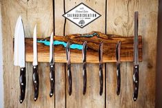 five knives are hanging on a wooden rack with blue paint in the center and black handles