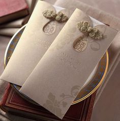 two wedding cards sitting on top of each other in front of a stack of books