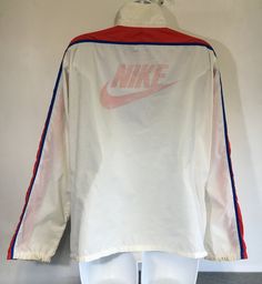 Here's a classic vintage Nike windbreaker! A large Nike logo is printed on back. The red, white, and blue color combo is perfect! There is a Nike tag inside the large front zipper pocket with the added bonus of being able to stuff the whole jacket into the pocket, zip it up, and peace out with your pouch! It shows some general wear---small marks, a hole at the pit seam, graphic wear, etc. But overall the fabric is in good condition and it has tons of fun left in it! Check out other sensational v Red Nylon Sportswear Track Jacket, Red Nylon Sporty Track Jacket, Red Nylon Track Jacket, Retro Nylon Track Jacket For Outdoor, Retro Track Jacket For Spring Sports, Retro White Track Jacket For Sports, Retro White Track Jacket For Outdoor, Retro Spring Track Jacket For Sports, Vintage Spring Sports Windbreaker