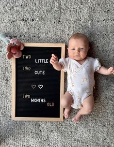 a baby laying on the floor next to a chalkboard with two little cute ones written on it