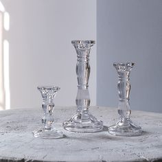 three clear glass candlesticks sitting on top of a white table next to each other