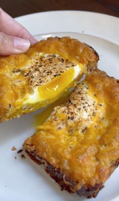 two pieces of food on a plate being held by a person's hand with an egg in the middle