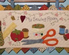 a quilt hanging on the wall with scissors and other items around it that says, my sewing room