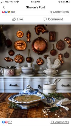 a table topped with lots of plates and bowls next to a wall covered in copper pans