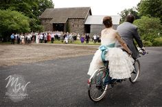 a bride and groom are riding on a bicycle in front of a large group of people