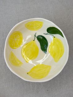 a white bowl with lemons painted on the side and green leaves in the middle