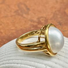 New, but old pieces, never worn, recently acquired from a premier jeweler located in Minneapolis, MN for many years- a rare opportunity! 18KT yellow Ggld genuine, bezel-set, white, oval, mabe pearl ring. Size 6.75 Sizable by us for a fee or your local jeweler Weight: 10.3 grams Band width: 3mm in back Pearl measures: 15mm x 11mm oval mabe pearl Stamped 18k By Honora Classic Oval Cabochon Dome Ring With Polished Finish, Timeless Oval Rings With High Luster, Timeless Oval Dome Ring For Formal Occasions, Antique Yellow Gold Oval Pearl Ring, Antique Oval Yellow Gold Pearl Ring, Classic Yellow Gold Oval Cabochon Jewelry, Timeless Gold Dome Ring With Cabochon, Timeless Yellow Gold Dome Ring With Cabochon, Classic Oval Cabochon Jewelry For Formal Occasions