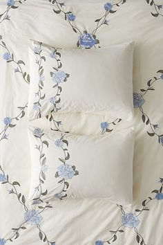 three pillows and two pillow cases on a bed with blue flowers in the background,