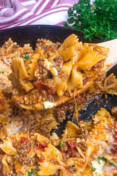 a skillet filled with pasta and meat being stirred by a wooden spoon over it