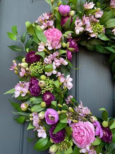 a wreath with purple flowers and green leaves on a gray front door, ready to be decorated for the holiday