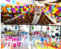 brightly colored tables and chairs are set up for an event with paper streamers hanging from the ceiling