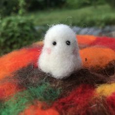 a small white bird sitting on top of a pile of colorful wooly material with trees in the background