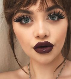 a woman with long lashes and dark lipstick on her face is wearing a necklace that has pearls hanging from it's sides