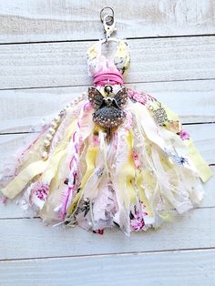 a dress keychain made out of fabric on a white wooden background with pink and yellow flowers