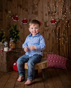 a young boy sitting on top of a wooden bench in front of a christmas tree