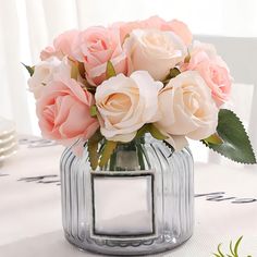 a glass vase filled with pink roses on top of a white tablecloth covered table