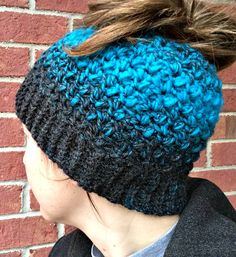 a woman wearing a blue and black crocheted headband with a ponytail in front of a brick wall