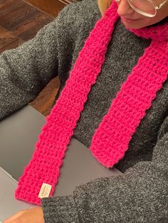 a woman wearing glasses and a pink knitted scarf is typing on a laptop computer