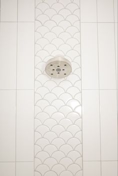 a shower head in the middle of a white tiled wall with fish scale designs on it