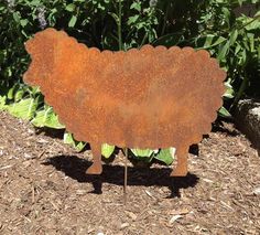 a rusted metal sheep sign sitting in the middle of a garden