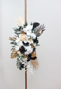 a white and black flower arrangement on a wooden stick with gold leaves in the center