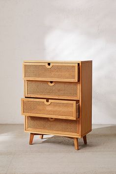 a wooden dresser with wicker drawers in front of a white wall and concrete floor