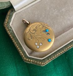 "A lovely antique antique locket, circa 1915-1920, with engraved swirls of leaves that float above delicate pearls, turquoise and paste. This locket has  such a soft and pretty palette of colors in golden yellow with splashes of soft blue and white. The sweeping swirls add the perfect amount of graceful texture to the overall design.  This locket opens up to reveal two photo holders with rose hued frames and closes to reveal the reverse engraved with the initials ULS.  Metal: Gold Fill Gemstones Turquoise Vintage Jewelry With Vintage Charm, Turquoise Locket For Wedding Jewelry, Turquoise Wedding Locket Jewelry, Turquoise Locket Jewelry For Wedding, Antique Medallion Pearl Pendant Jewelry, Turquoise Round Locket Jewelry, Round Turquoise Locket Jewelry, Turquoise Medallion Locket Jewelry, Turquoise Round Pendant Locket Jewelry