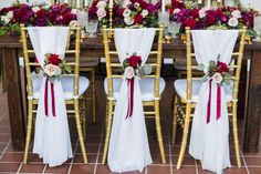 the chairs are covered with white linens and red sashes, along with burgundy flowers