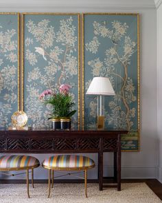 two chairs and a table in front of a wall with paintings on the wall behind it