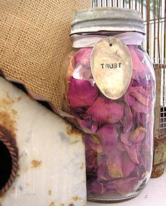 a jar filled with pink flowers sitting on top of a table next to a pillow