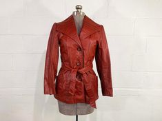 Bust: 34" Waist: 28" Hips: 38" Length: 26" Sleeve Length: 22" Material: leather with a satin lining Brand: none listed Killer reddish brown button front leather jacket with a tie waist. There are two front pockets and large collar. Coat is in good shape and lined with a satin-like fabric. There are a few faint spots on the leather likely from age and wear. Fabric has NO stretch.  ✂ All garments measured laying flat. Bust, waist, & hip measurements are already doubled. Please refer to the last photo for the size chart I use to determine modern sizing. ✂ Please zoom in on photos for a better view of the item's condition. All items are vintage and pre-loved. All major flaws are listed, but small blemishes like loose stitches and buttons may not be in the item description as they are to be exp Fitted Retro Leather Jacket For Fall, Retro Fitted Leather Jacket For Fall, Vintage Double-breasted Leather Jacket For Fall, Fitted Vintage Brown Retro Leather Jacket, Fitted Retro Vintage Brown Leather Jacket, Retro Single-breasted Leather Jacket For Fall, Vintage Fitted Button-up Leather Jacket, Retro Fitted Leather Jacket, Vintage Fitted Leather Jacket For Work